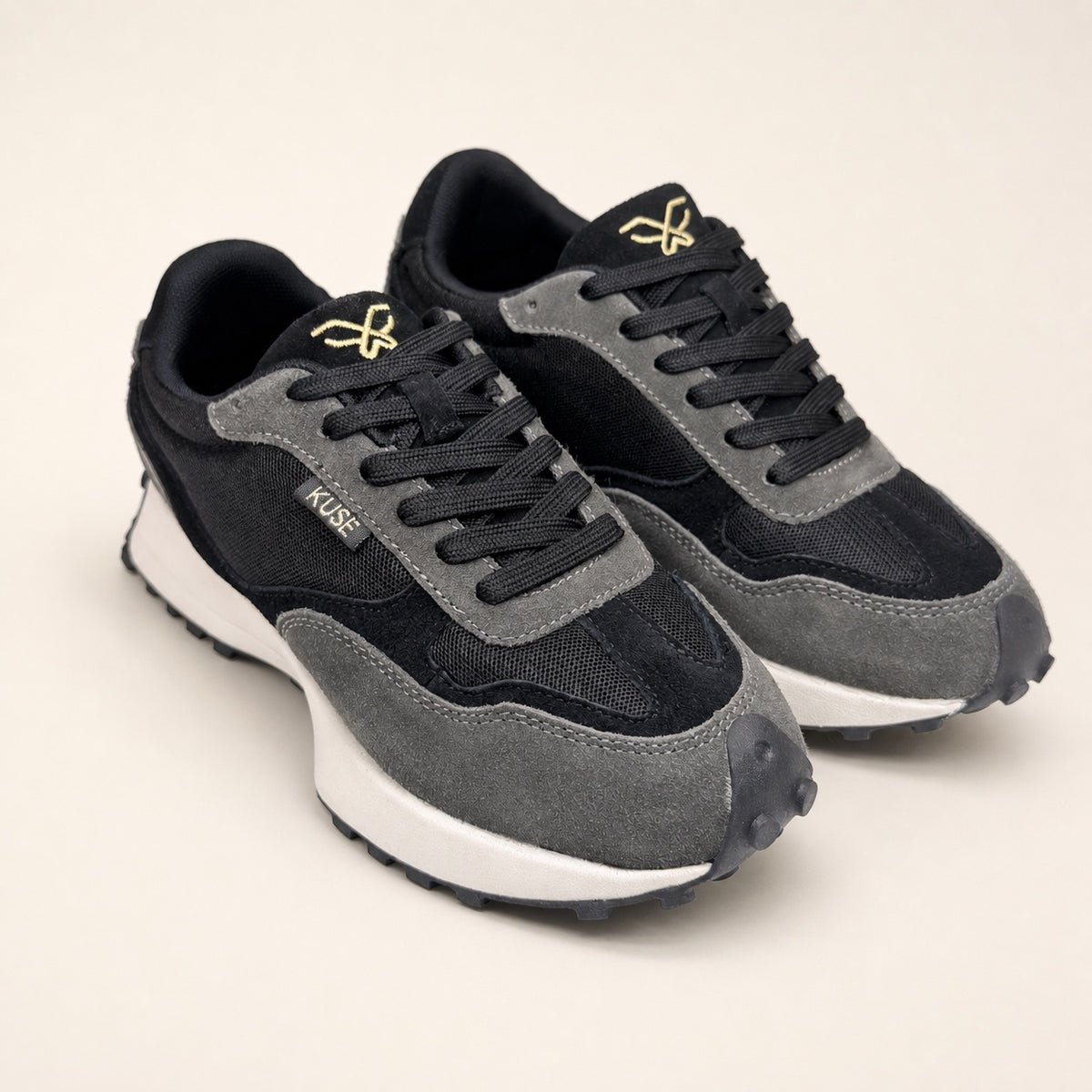 Vista tres cuartos par zapatillas Kuse negras con logo dorado y diseño retro contemporáneo