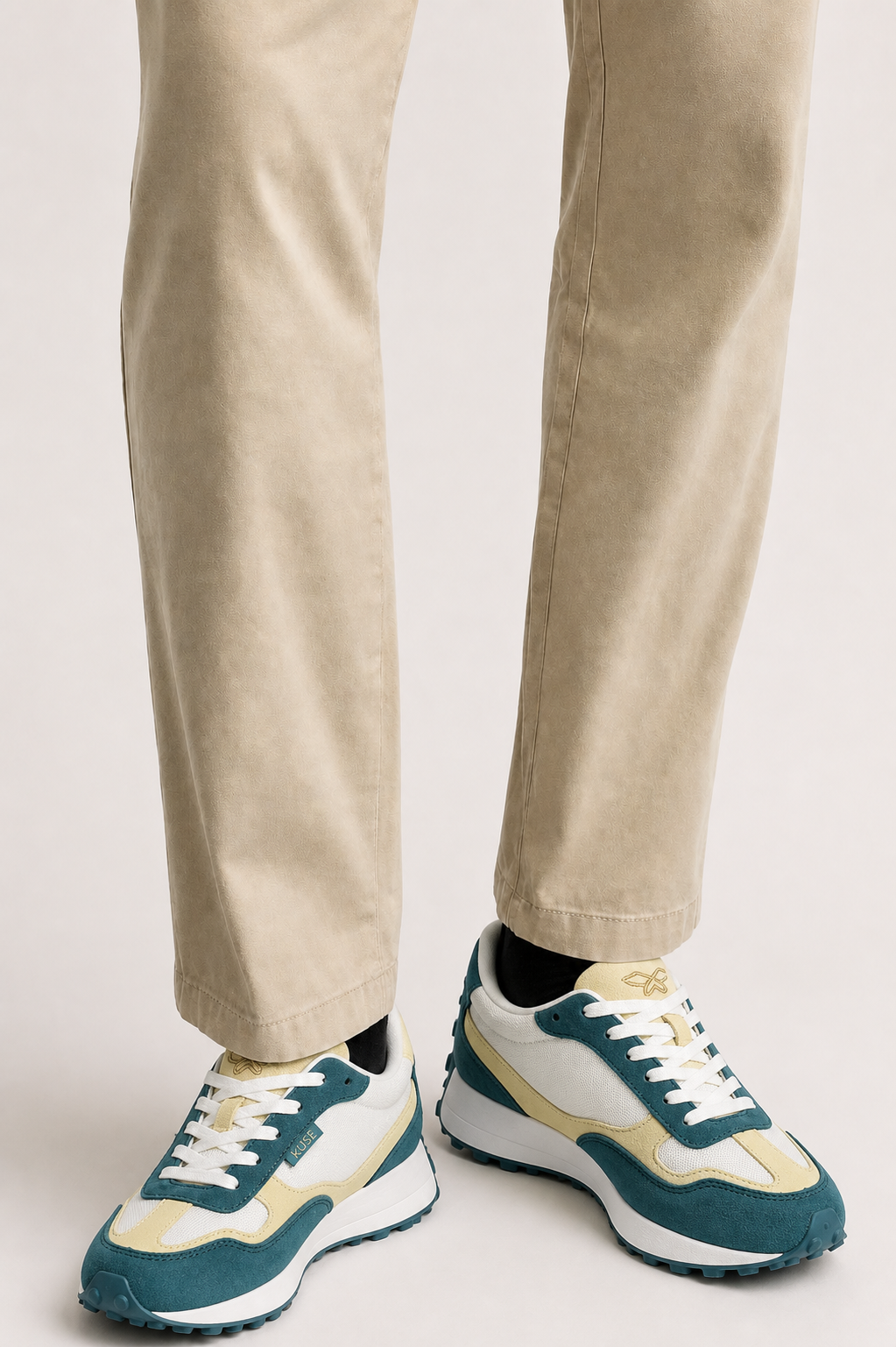 Primer plano de zapatillas deportivas KUSE verde malaquita y crema combinadas con pantalón beige.