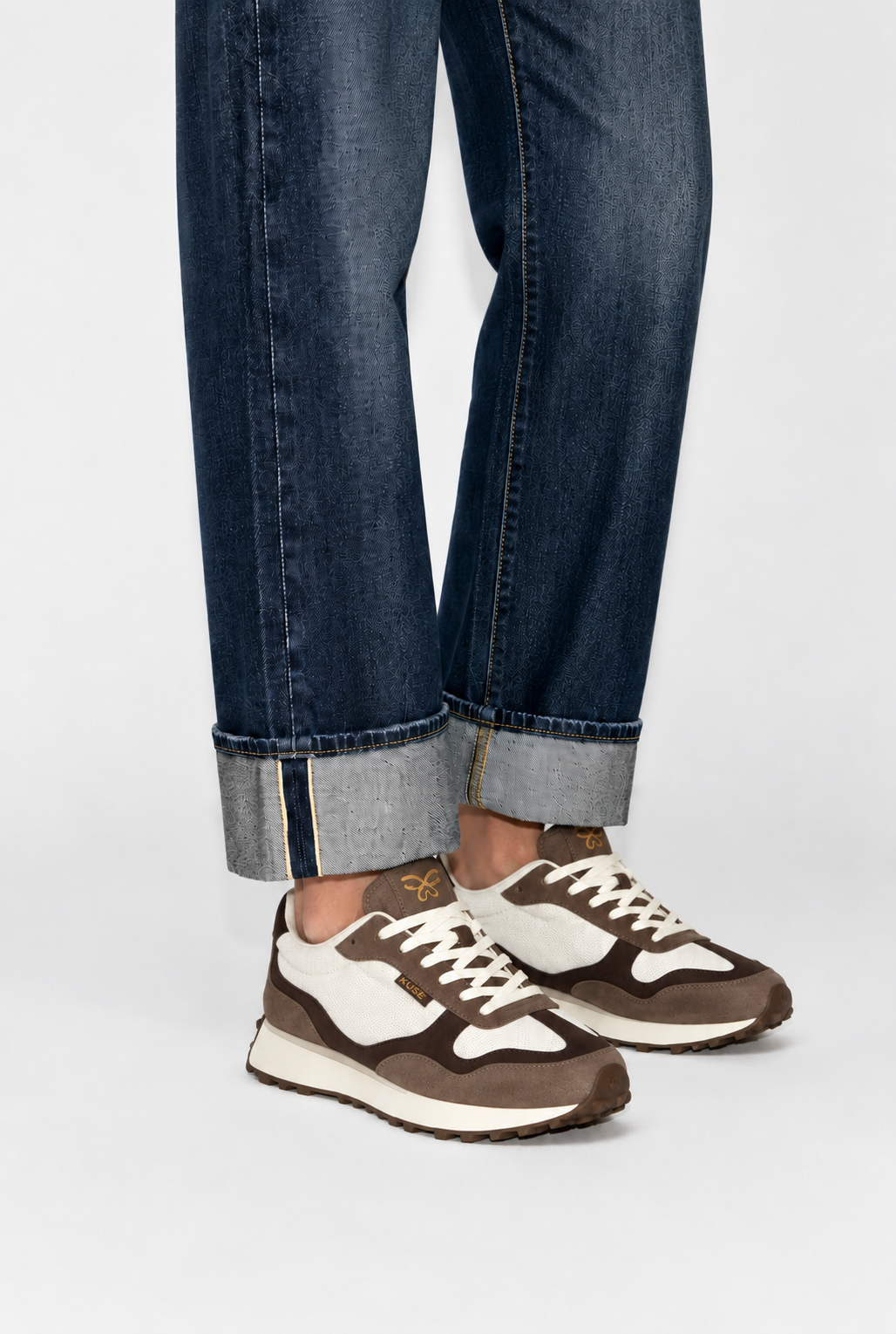 Detalle de zapatillas casual unisex marrón y burdeos combinadas con jeans oscuros