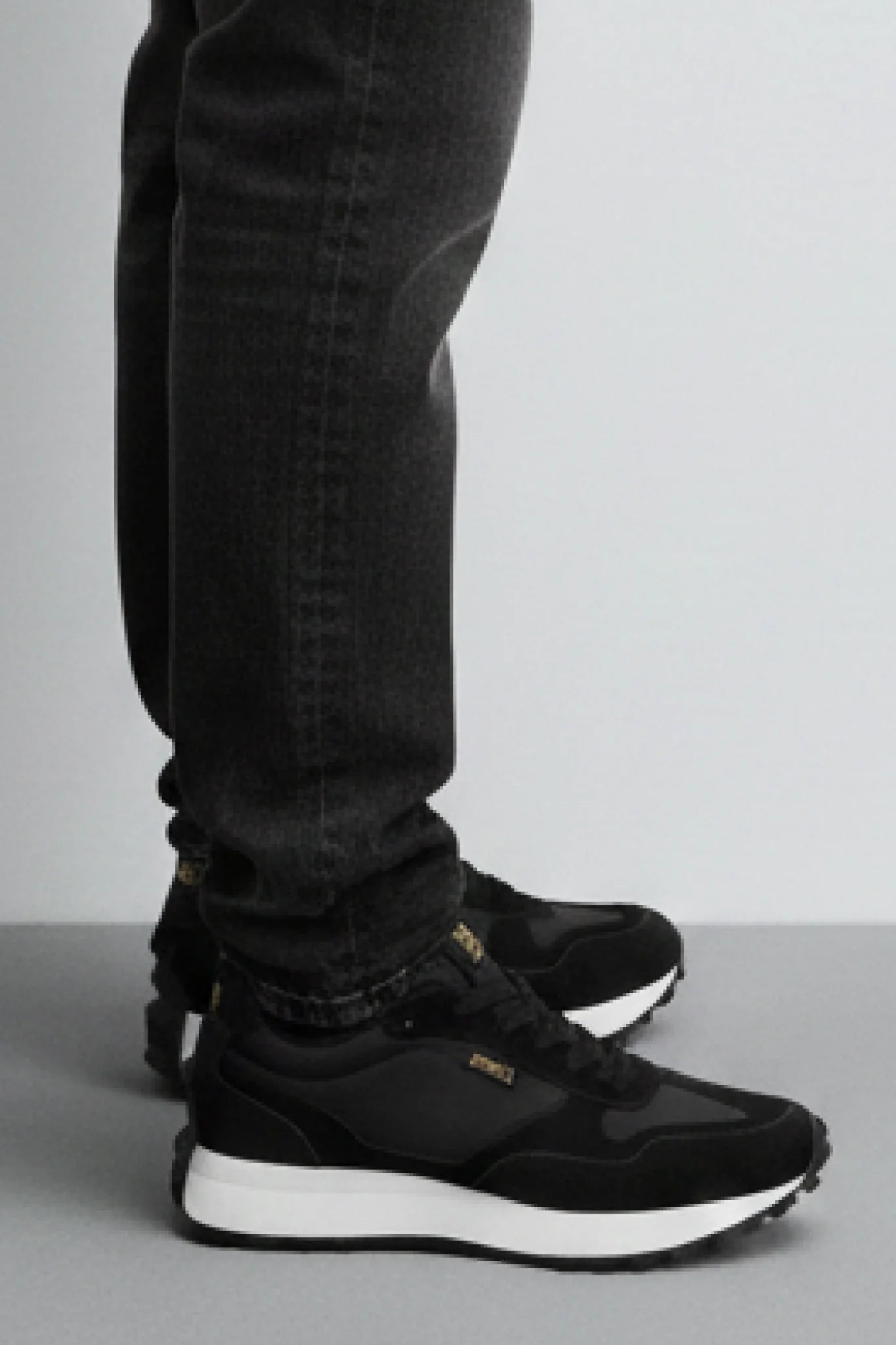 Detalle zapatillas Kuse negras unisex con jeans oscuros y suela blanca de contraste